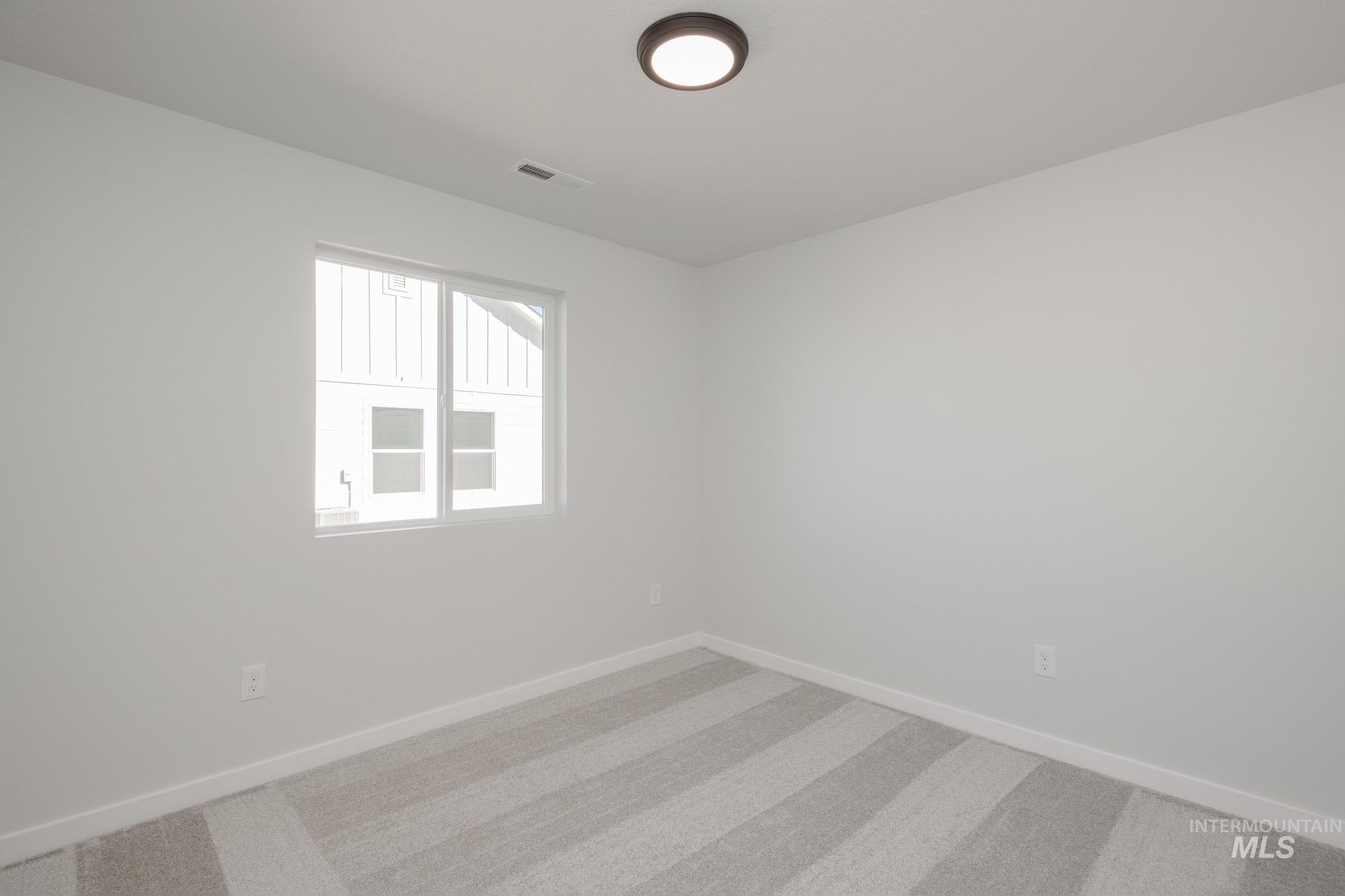 14092 Shiny Spruce Street Caldwell, ID 83607 - Photo 16 of 22 Bright room featuring a large window, neutral wall paint, striped carpet, white baseboards, and a flush-mount ceiling light