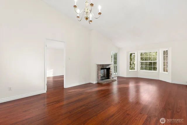 an empty room with wooden floor chandelier and windows