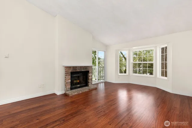 an empty room with wooden floor fireplace and windows