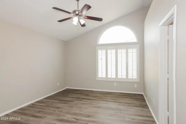 an empty room with wooden floor chandelier fan and windows
