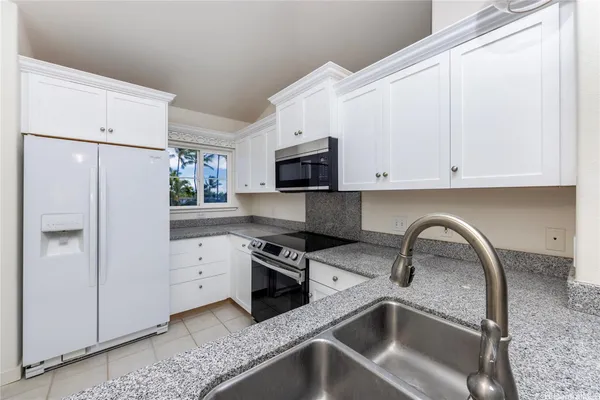 a kitchen with granite countertop a sink and a stove top oven with white cabinets