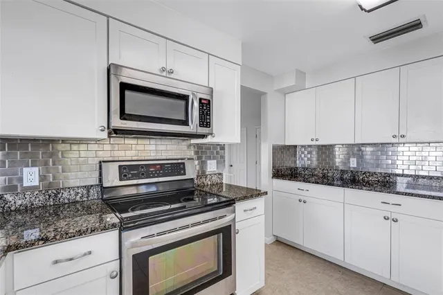 a kitchen with granite countertop a refrigerator and white cabinets
