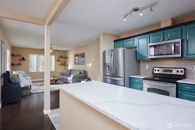 a kitchen with stainless steel appliances kitchen island granite countertop a refrigerator a stove a sink dishwasher a oven with couches and flat screen tv