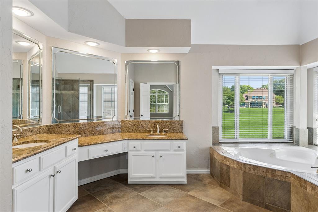 2925 Sunset Ridge McKinney, TX 75072 - Photo 25 of 33 Elegant spa-inspired primary bathroom featuring dual granite vanities, expansive mirrors, custom cabinetry, designer lighting, corner soaking tub, and beautiful golf course views that create a serene luxury retreat.