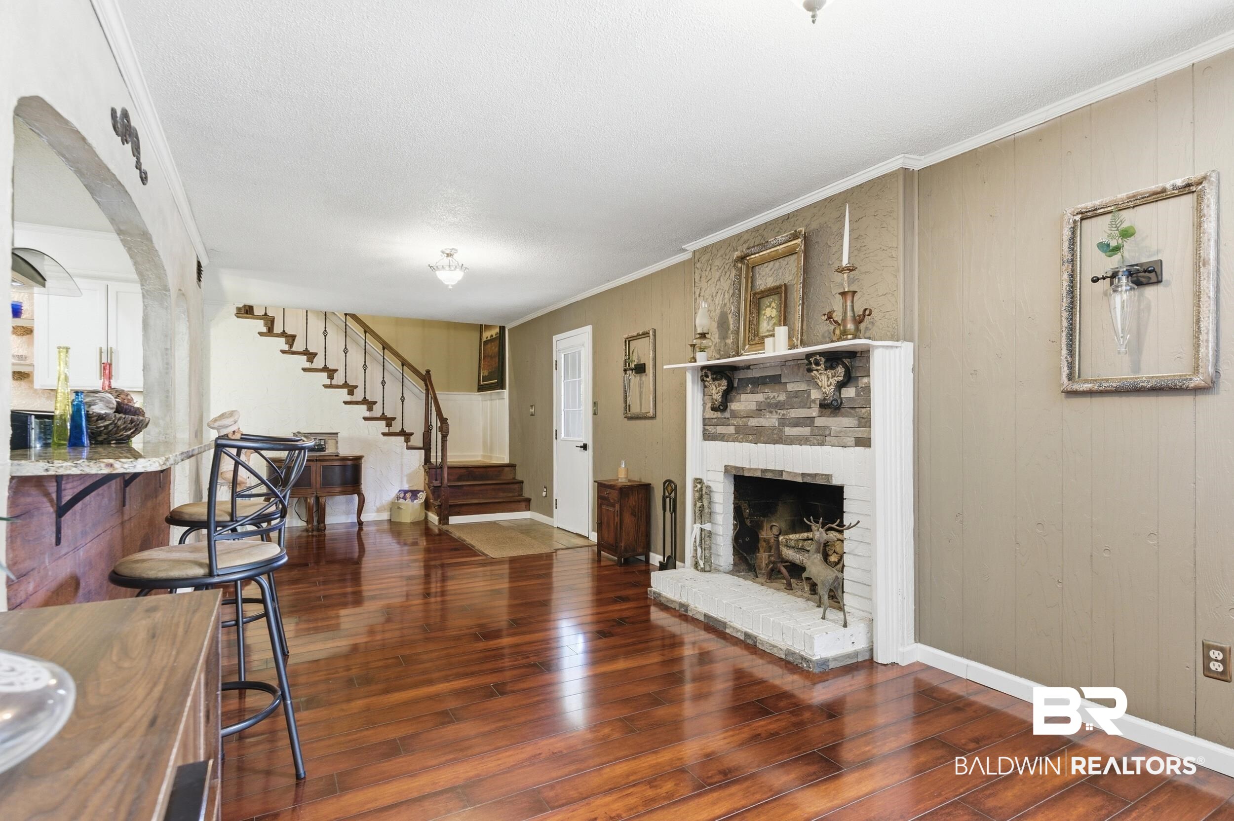 51620 Robert White Road Bay Minette, AL 36507 - Photo 20 of 81 Spacious living area featuring polished wood-finish flooring, a brick-front fireplace with a white mantel, and a staircase with dark wood treads and wrought iron balusters