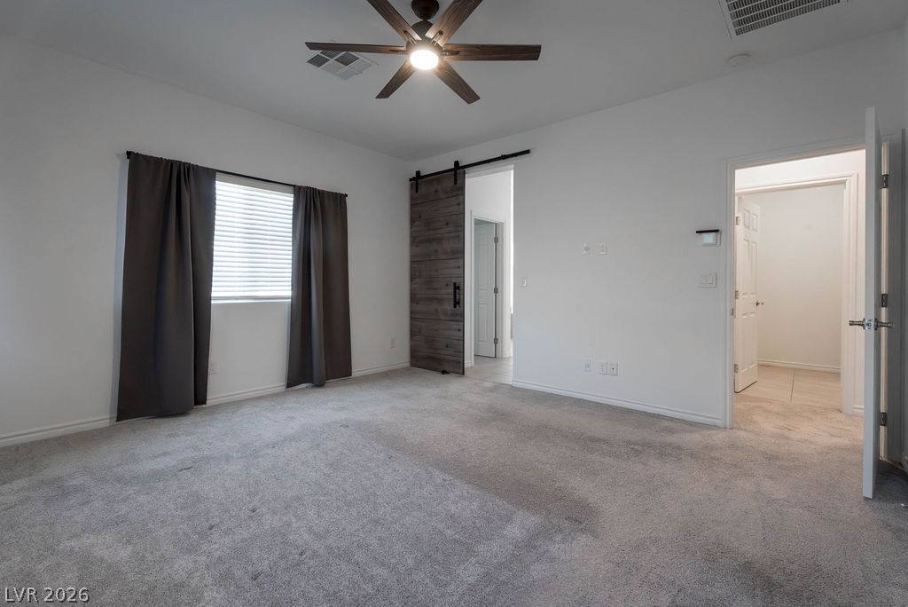 7126 Calvert Cliffs Street North Las Vegas, NV 89084 - Photo 21 of 44 A well-lit bedroom with a ceiling fan, featuring a modern barn door leading to an adjacent space.