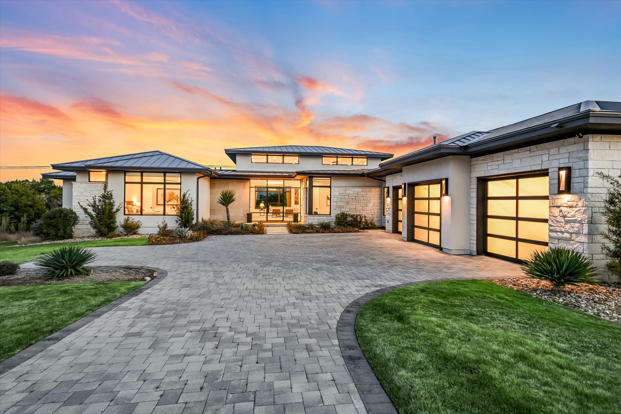 View of front of house with a standing seam roof, curved driveway, stone siding, and a lawn