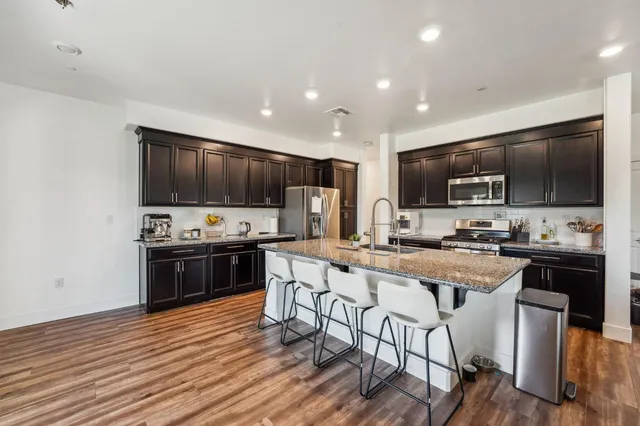 a kitchen with stainless steel appliances a stove top oven a sink dishwasher a refrigerator and a dining table with wooden floor