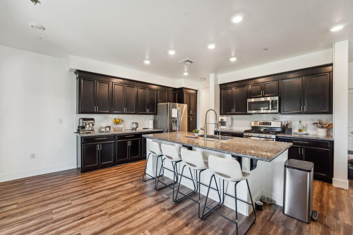 2074 Abbeylane Way Olivehurst, CA 95961 - Photo 5 of 39 a kitchen with stainless steel appliances a stove top oven a sink dishwasher a refrigerator and a dining table with wooden floor