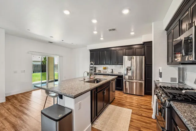 a kitchen with stainless steel appliances granite countertop a stove top oven a sink dishwasher and a refrigerator with wooden floor