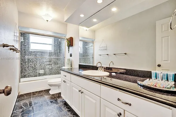 a spacious bathroom with a granite countertop sink a toilet a mirror and a shower