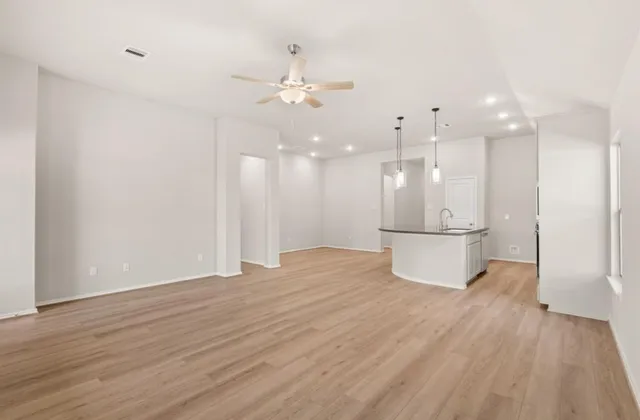 a view of an empty room and kitchen view with wooden floor