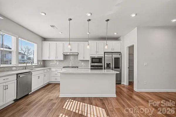 a large kitchen with stainless steel appliances kitchen island granite countertop a refrigerator a stove a sink and white cabinets with wooden floor