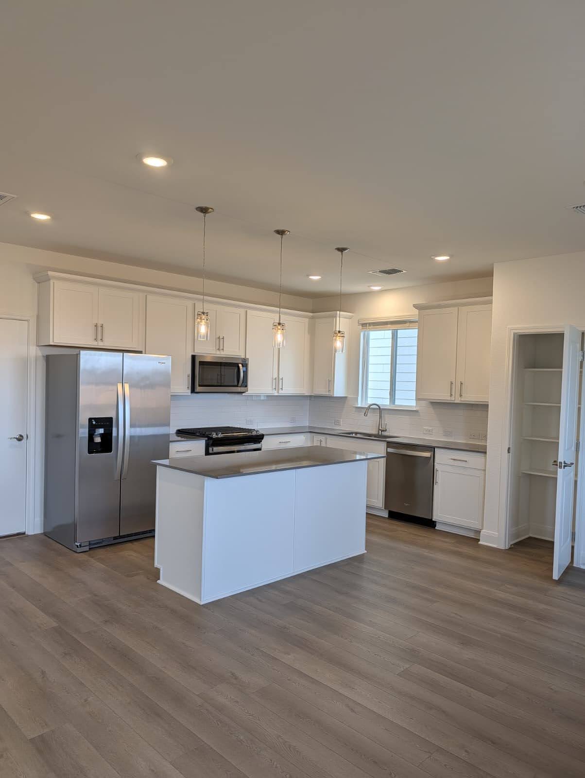 212 Daniels Dusty Trail Georgetown, TX 78626 - Photo 7 of 23 Kitchen featuring appliances with stainless steel finishes, white cabinetry, decorative light fixtures, a kitchen island, and dark wood-type flooring