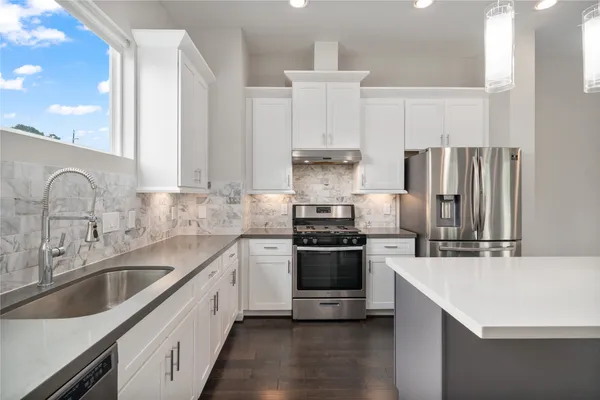 a kitchen with stainless steel appliances granite countertop a sink a stove a refrigerator and white cabinets with wooden floor