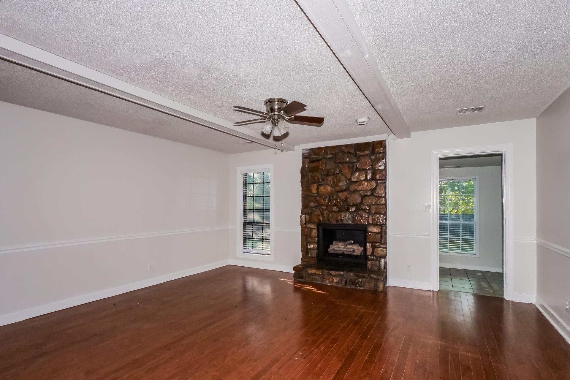 1441 Sandy Stone Lane Memphis, TN 38016 - Photo 11 of 18 Unfurnished living room with beam ceiling, a textured ceiling, dark wood-style flooring, ceiling fan, and a fireplace