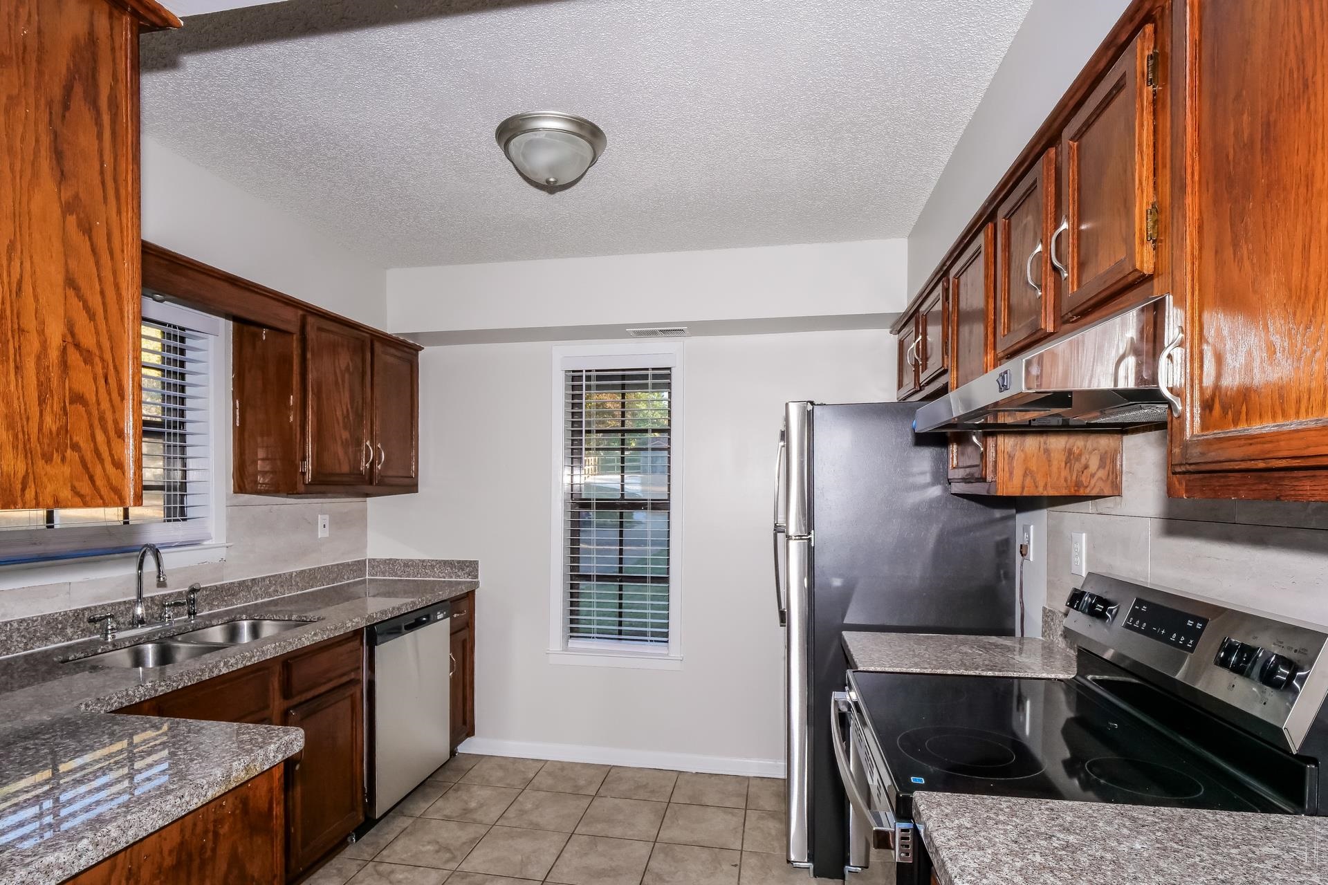1441 Sandy Stone Lane Memphis, TN 38016 - Photo 3 of 18 Kitchen featuring stainless steel appliances, a textured ceiling, under cabinet range hood, light tile patterned flooring, and dark stone countertops