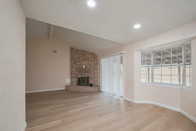 an empty room with wooden floor fireplace and windows