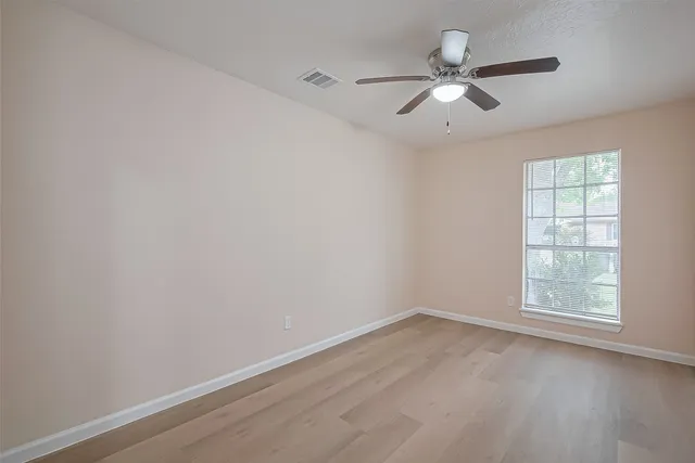an empty room with wooden floor ceiling fan and windows