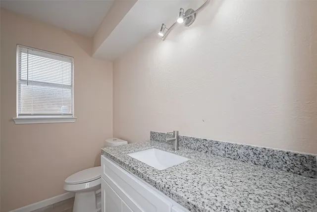a bathroom with a granite countertop sink a toilet and a window