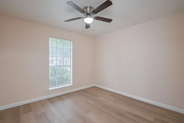 an empty room with wooden floor ceiling fan and windows