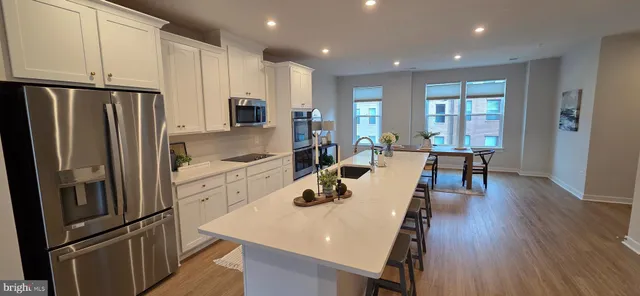 a kitchen with stainless steel appliances a refrigerator a stove a dining table and chairs with wooden floor