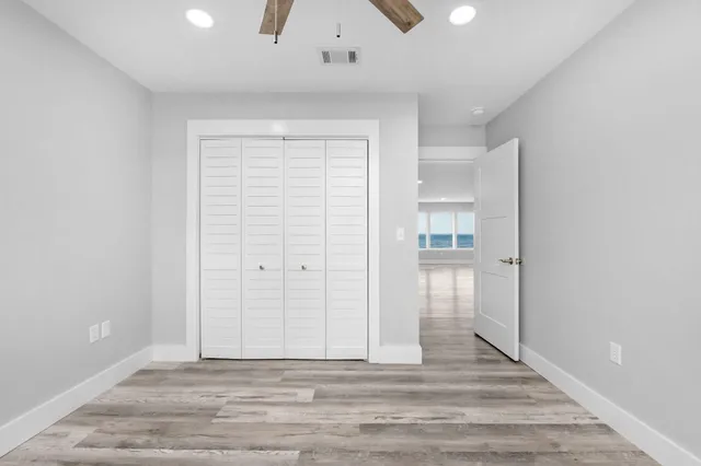 an empty room with wooden floor chandelier fan and windows