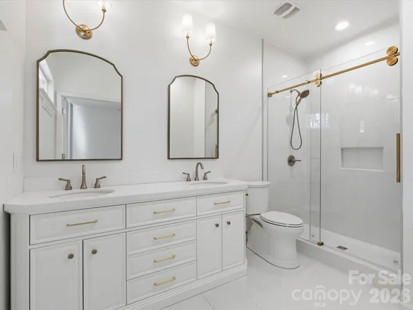 a bathroom with double vanity a toilet a mirror and vanity