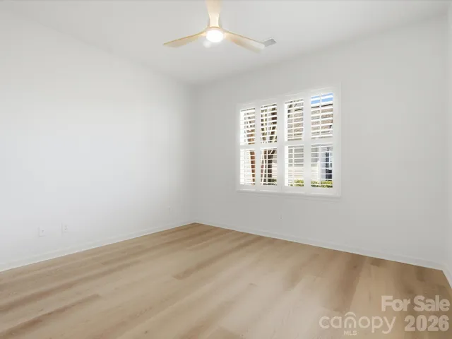 an empty room with wooden floor ceiling fan and windows