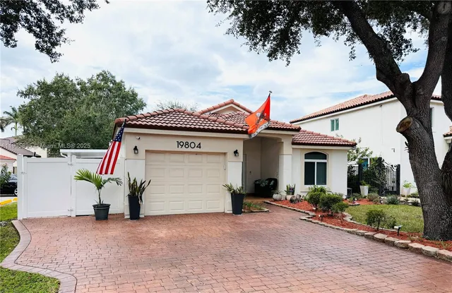 a view of a white house with a small yard and a large tree