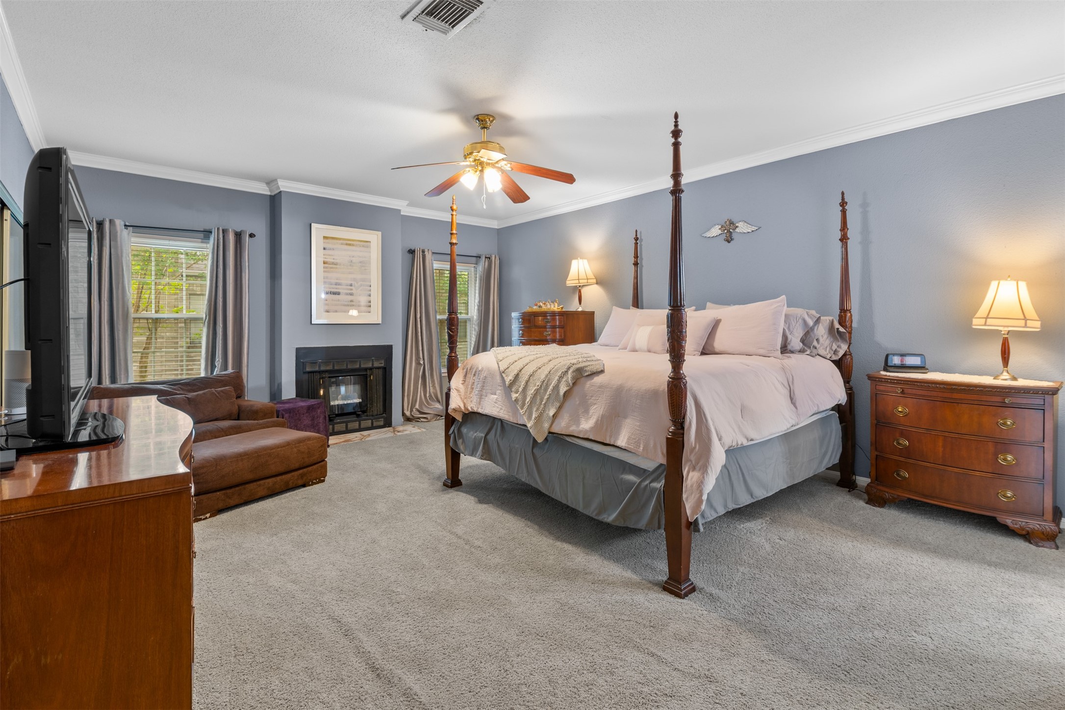 6000 Reims Road, Unit 2307 Houston, TX 77036 - Photo 12 of 26 Spacious bedroom with a fireplace, a large, elegant four-poster bed that fits comfortably, and plush carpet. Large windows provide natural light, complemented by a ceiling fan and tasteful decor for a retreat-like atmosphere.
