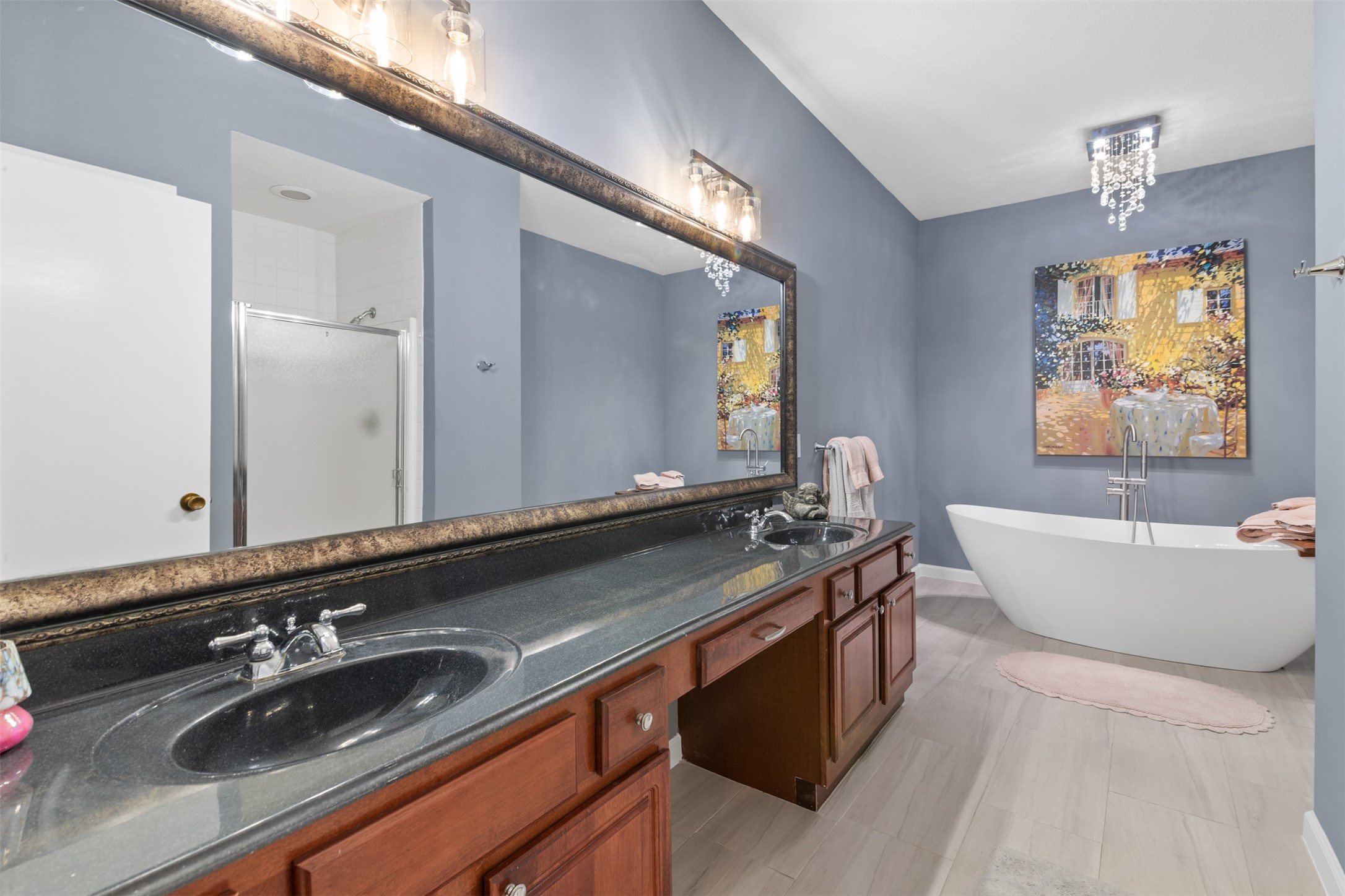 6000 Reims Road, Unit 2307 Houston, TX 77036 - Photo 14 of 26 This bathroom features a modern design with a freestanding tub, dual sinks, and a large mirror. The space is enhanced by elegant lighting, a spacious shower, and stylish decor, creating a relaxing and luxurious atmosphere.