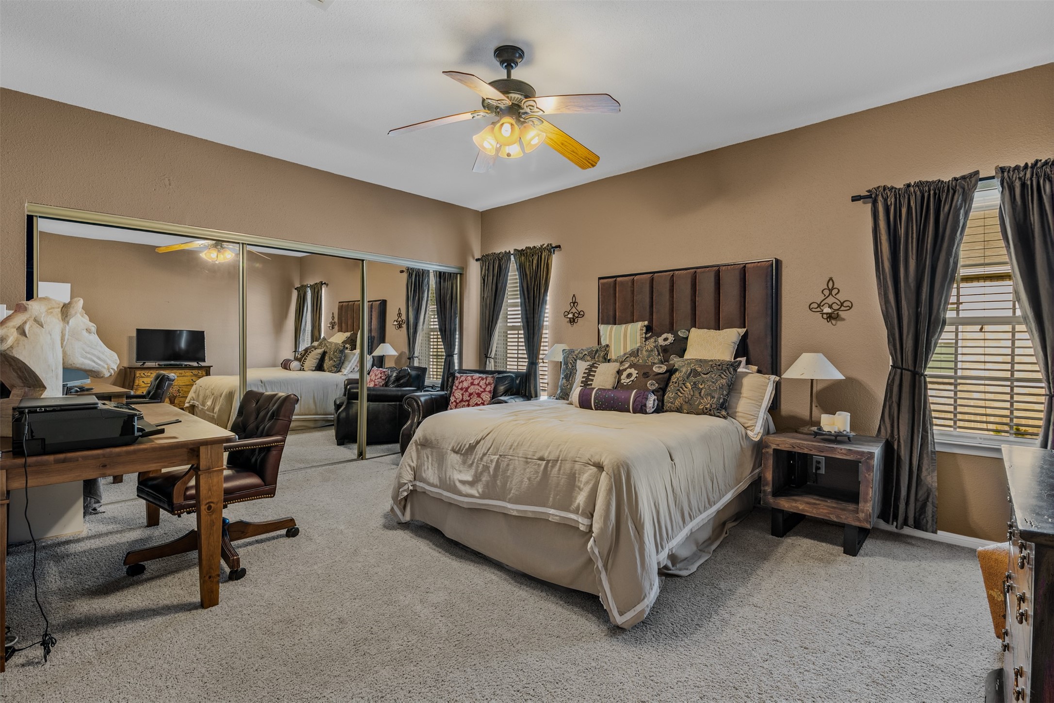 6000 Reims Road, Unit 2307 Houston, TX 77036 - Photo 18 of 26 Spacious bedroom with carpet, a ceiling fan, and abundant natural light. Features a large mirrored closet, elegant curtains, and space for a desk area.