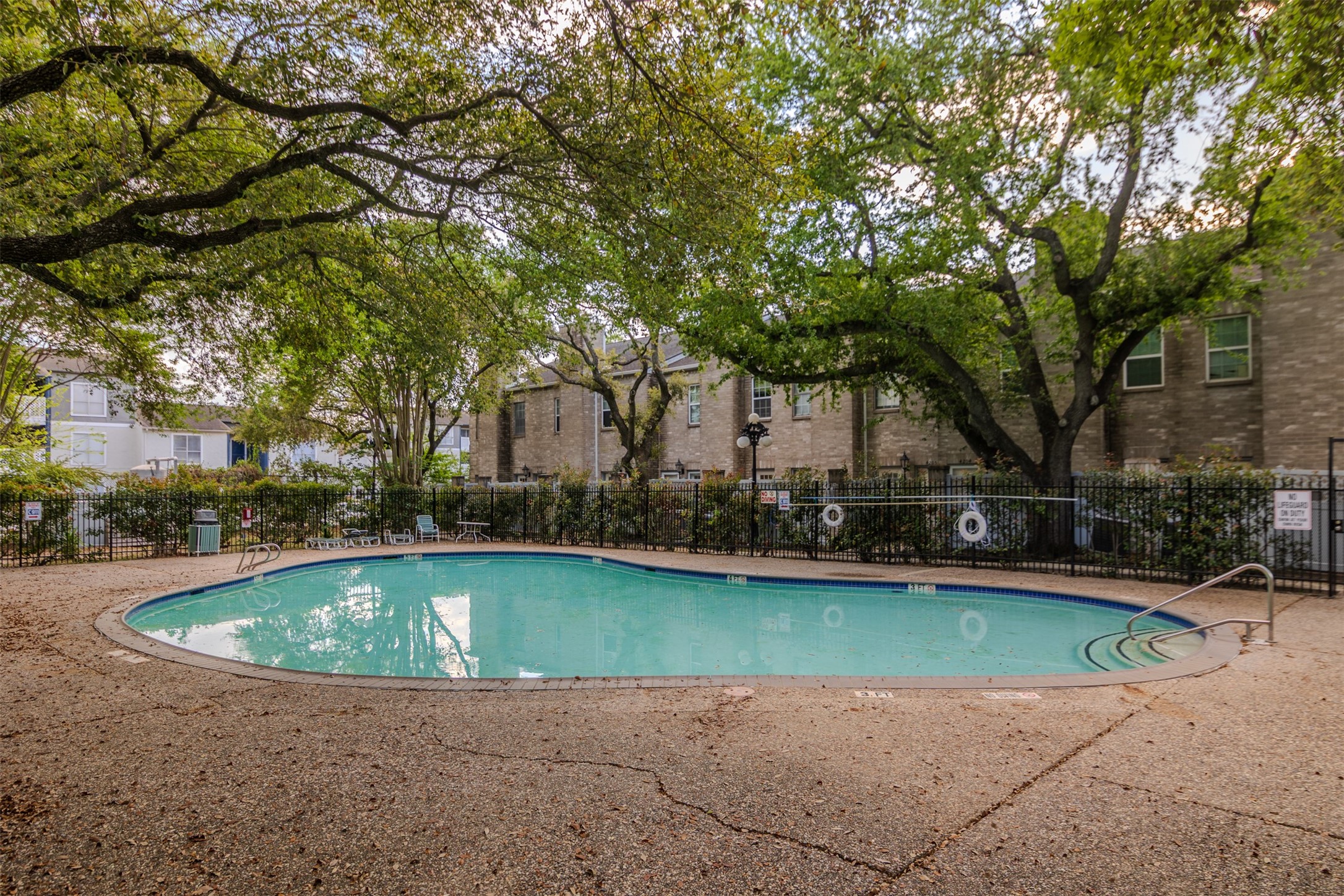 6000 Reims Road, Unit 2307 Houston, TX 77036 - Photo 21 of 26 A serene outdoor pool surrounded by mature trees and a secure fence, providing a relaxing and private atmosphere for residents.