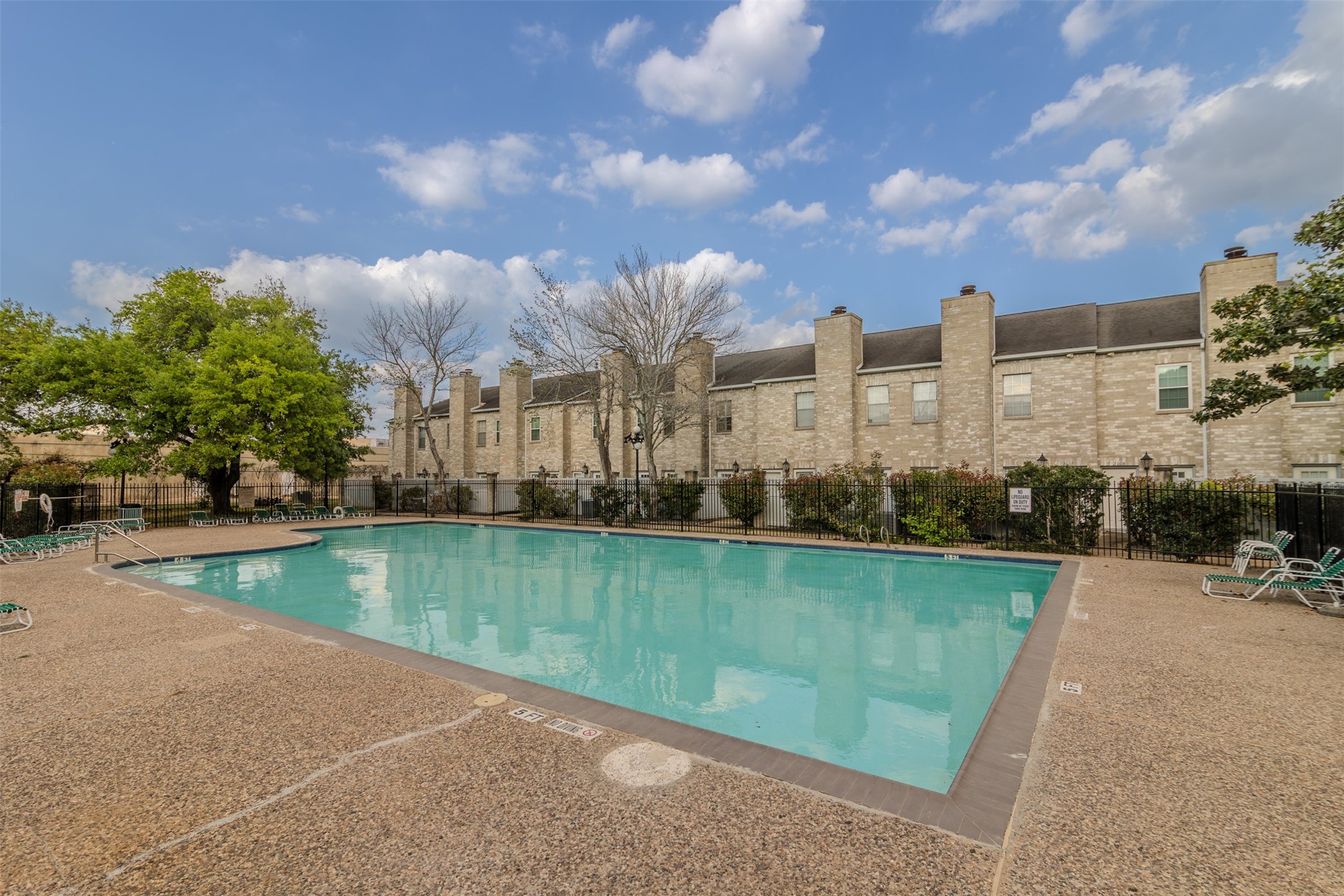 6000 Reims Road, Unit 2307 Houston, TX 77036 - Photo 22 of 26 Another community pool with a surrounding patio area, set against the backdrop of a row of charming townhouses. The area is fenced and includes lounge chairs, making it ideal for relaxation and leisure.