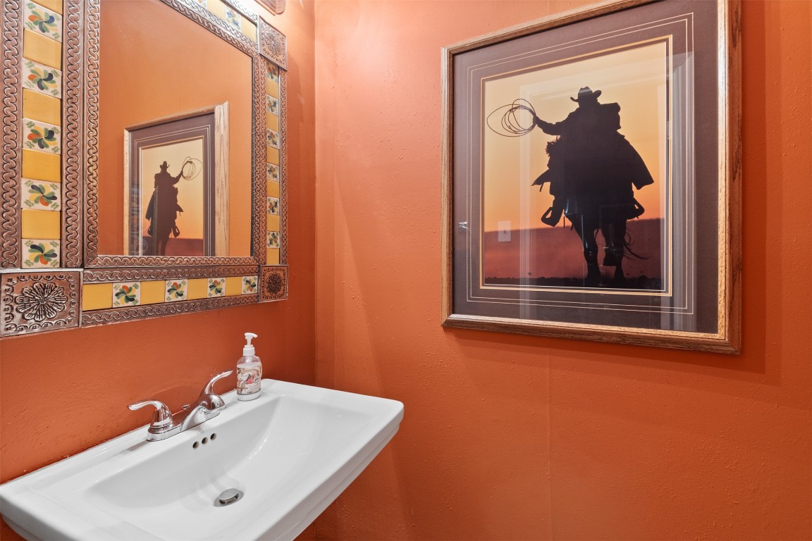 6000 Reims Road, Unit 2307 Houston, TX 77036 - Photo 10 of 26 Cozy powder room with warm orange walls, a stylish framed cowboy artwork, and a decorative mirror with colorful tile accents above a sleek white sink.