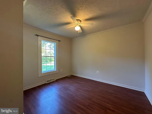 an empty room with wooden floor fan and windows