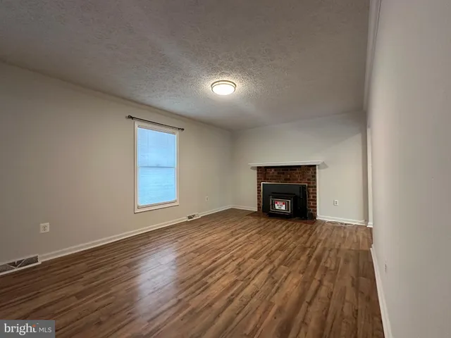 a view of an empty room with wooden floor fireplace and a window