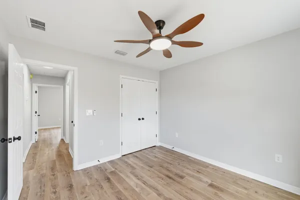an empty room with wooden floor fan and windows