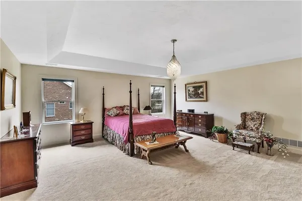 a spacious bedroom with a bed a chandelier and dresser