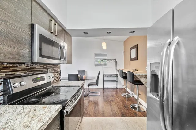 a kitchen with stainless steel appliances granite countertop a refrigerator a stove and a wooden floor