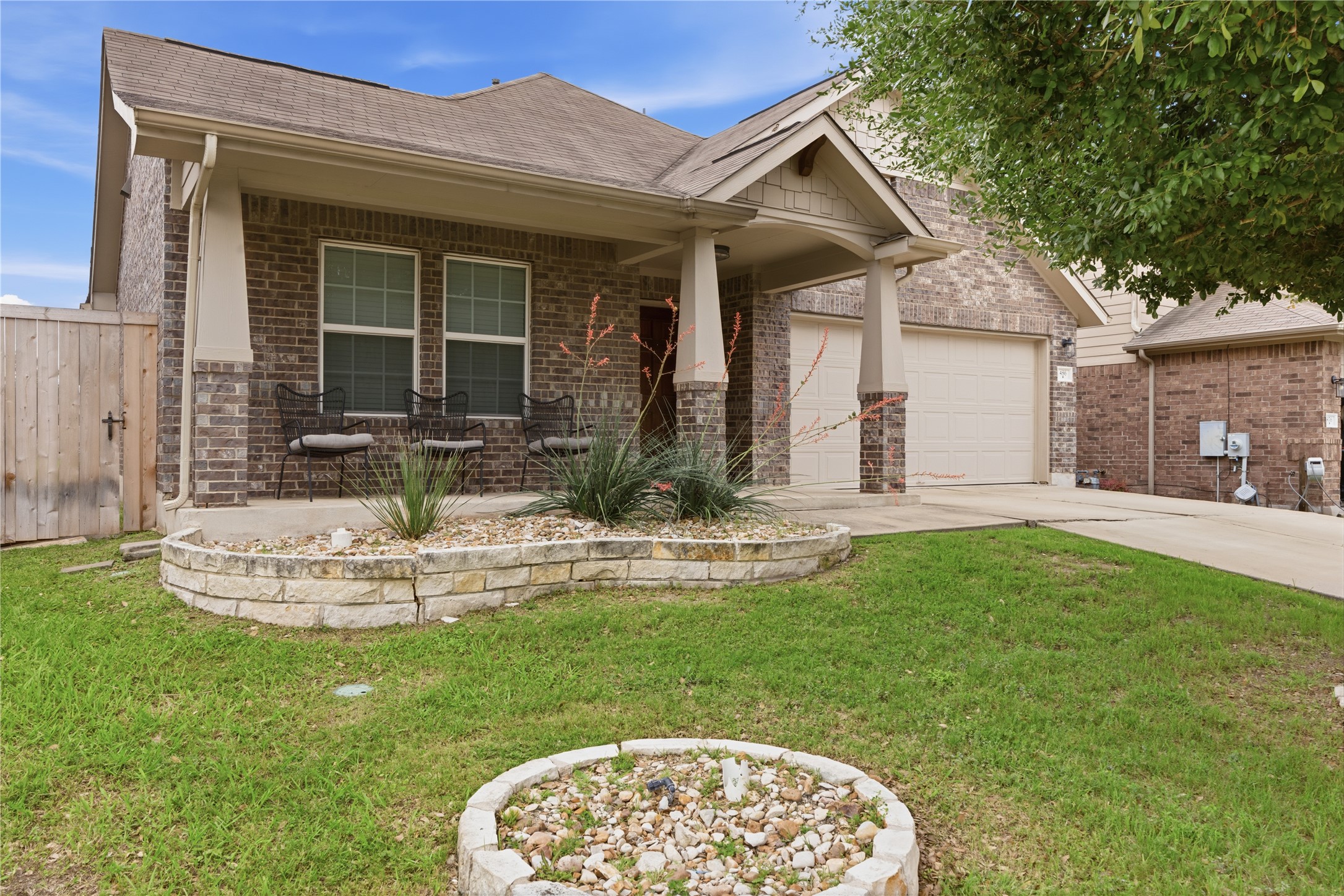 486 Pond View Pass Buda, TX 78610 - Photo 2 of 39 Brick and stone exterior featuring a covered porch, an attached two-car garage, a concrete driveway, a stone-lined planter bed, and a wooden privacy fence