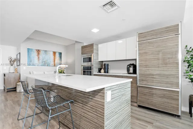 a large kitchen with kitchen island a sink a stove a refrigerator a dining table and chairs with wooden floor