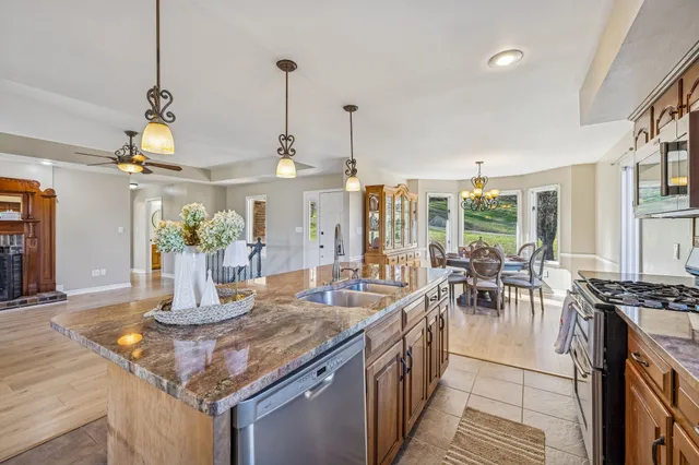 a kitchen with stainless steel appliances granite countertop a refrigerator a oven a sink a stove and a dining table with wooden floor