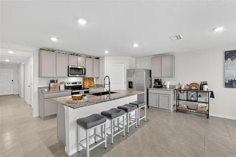a large white kitchen with stainless steel appliances granite countertop a stove a sink a refrigerator and white cabinets