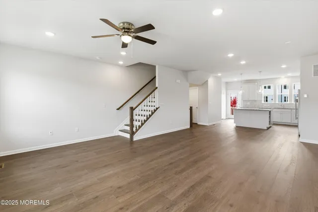 a view of an empty room with wooden floor and a ceiling fan