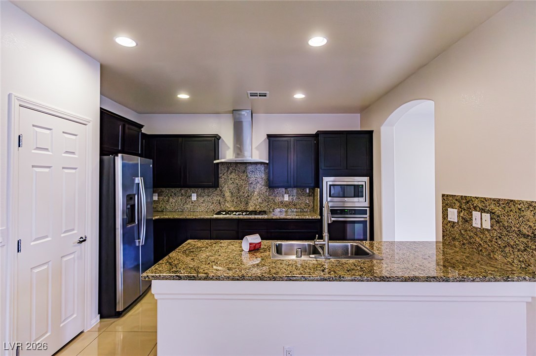 11009 Ketchikan Street Las Vegas, NV 89179 - Photo 9 of 59 Kitchen with decorative backsplash, a peninsula, appliances with stainless steel finishes, wall chimney range hood, and recessed lighting