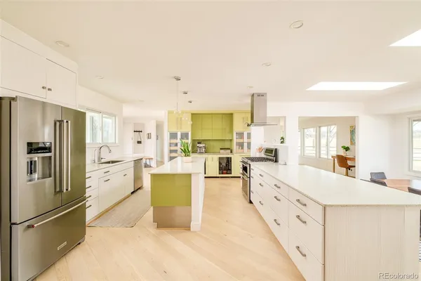 a large kitchen with kitchen island a refrigerator a sink dishwasher a stove and white cabinets with wooden floor