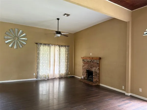 an empty room with wooden floor fireplace and windows