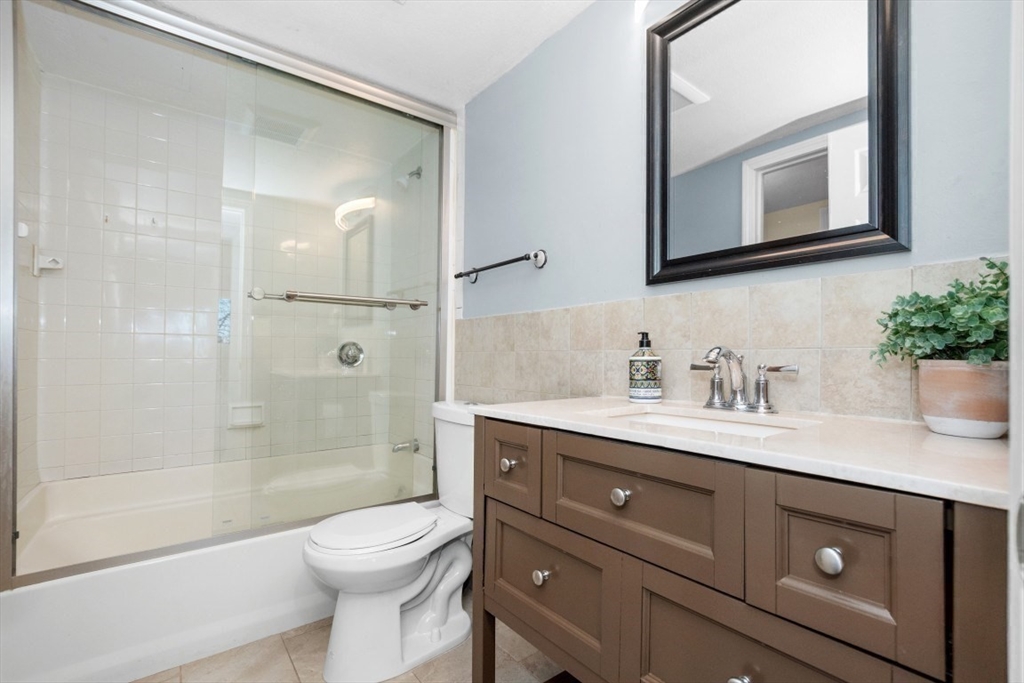 165 Cottage Street, Unit 410 Chelsea, MA 02150 - Photo 11 of 25 a bathroom with a granite countertop toilet a sink a mirror a shower and vanity
